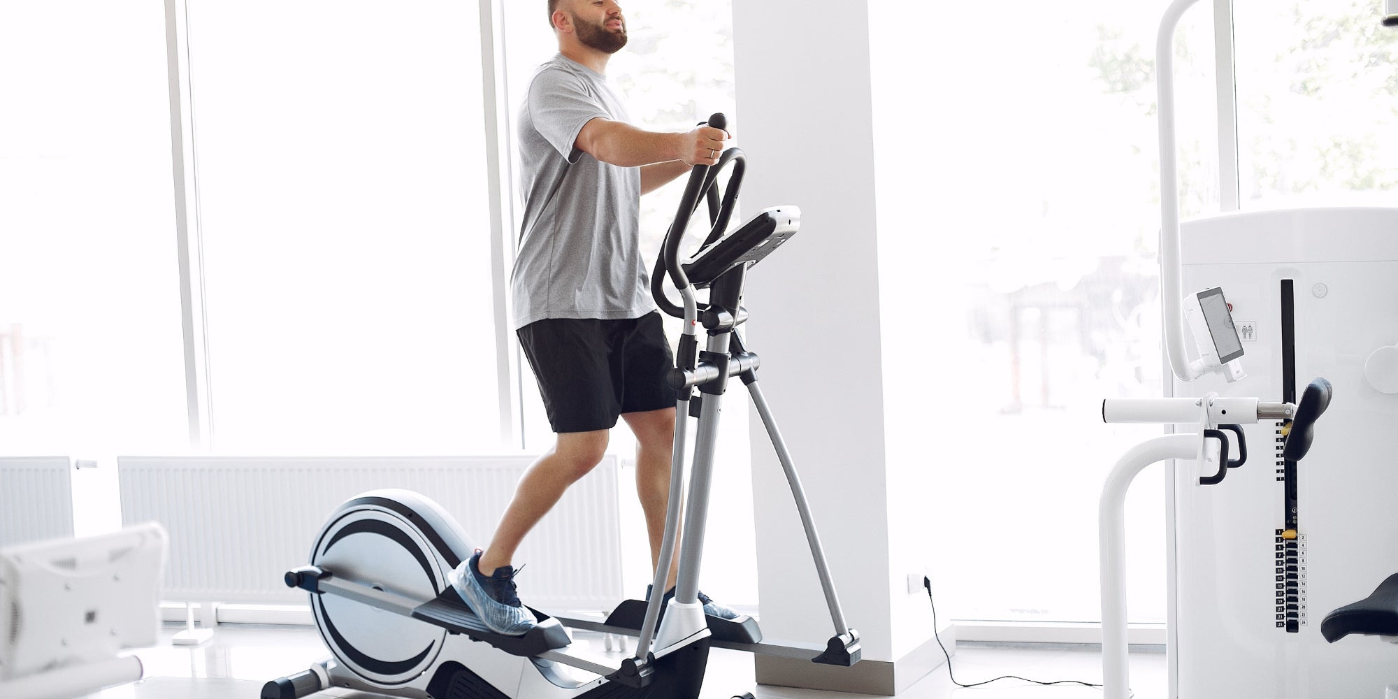Man exercising on an elliptical machine in a gym setting

