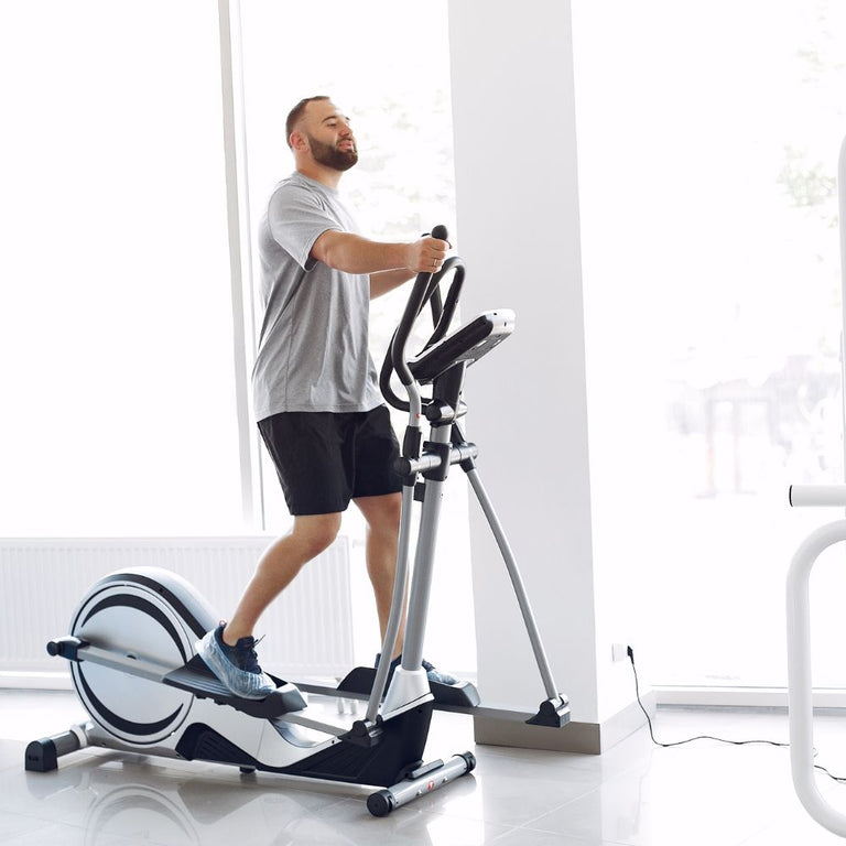 Man exercising on an elliptical machine in a gym setting

