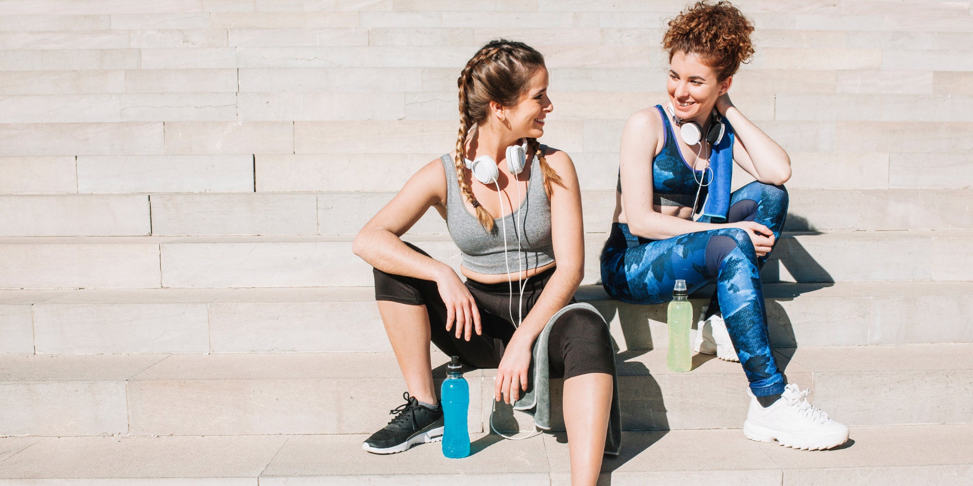 Two women sitting on stone steps after a workout, with exercise equipment around them.

