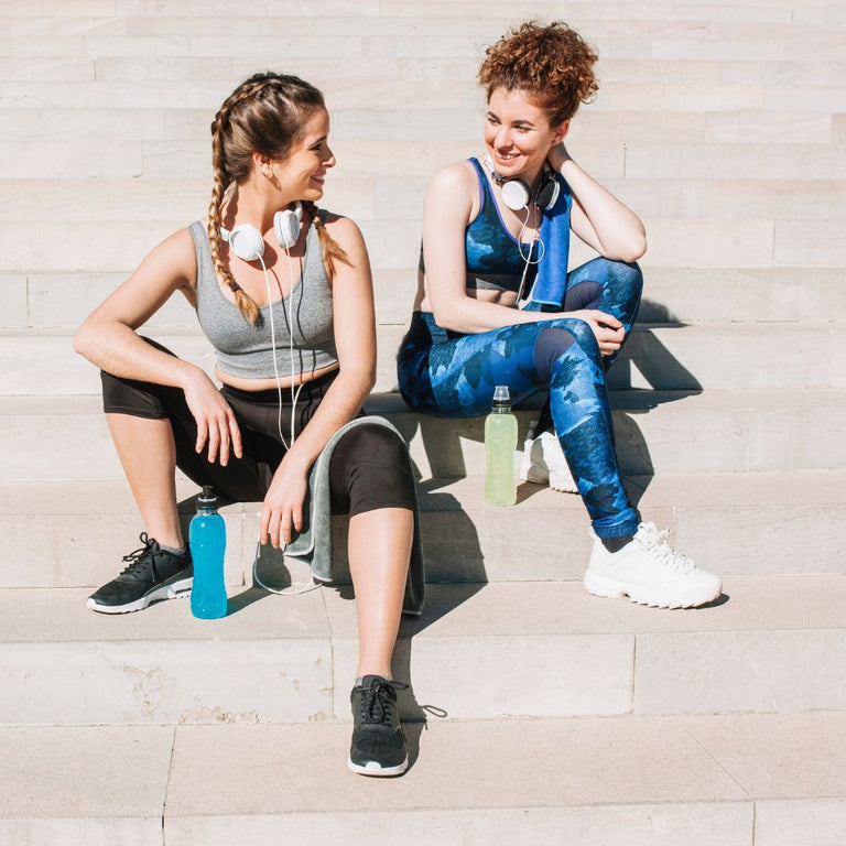Two women sitting on stone steps after a workout, with exercise equipment around them.

